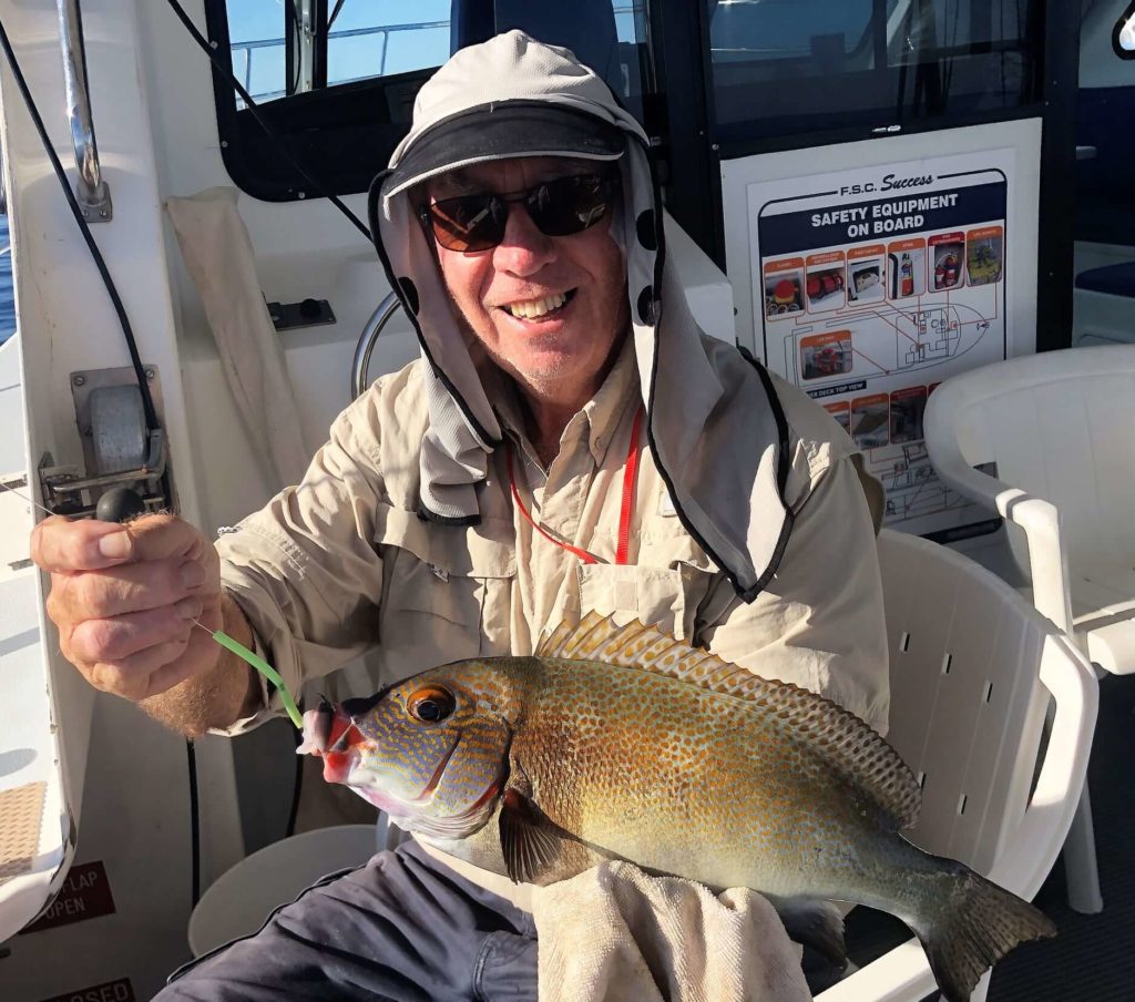 Headshot of man wearing hat and sunglasses holding fish in one hand