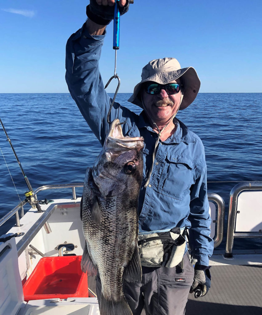 Man holding fish by hook on boat on ocean